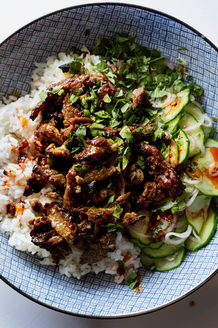 Garlic and black pepper beef in a bowl with rice and cucumbers.