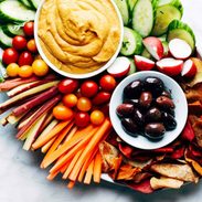 Plates of hummus and olives on a pile of vegetables.