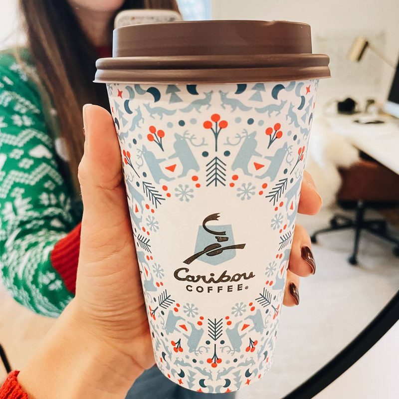 White woman holding holiday themed coffee cup.