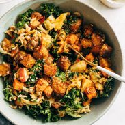 Crispy tempeh with green leafy vegetables in a bowl with a spoon.