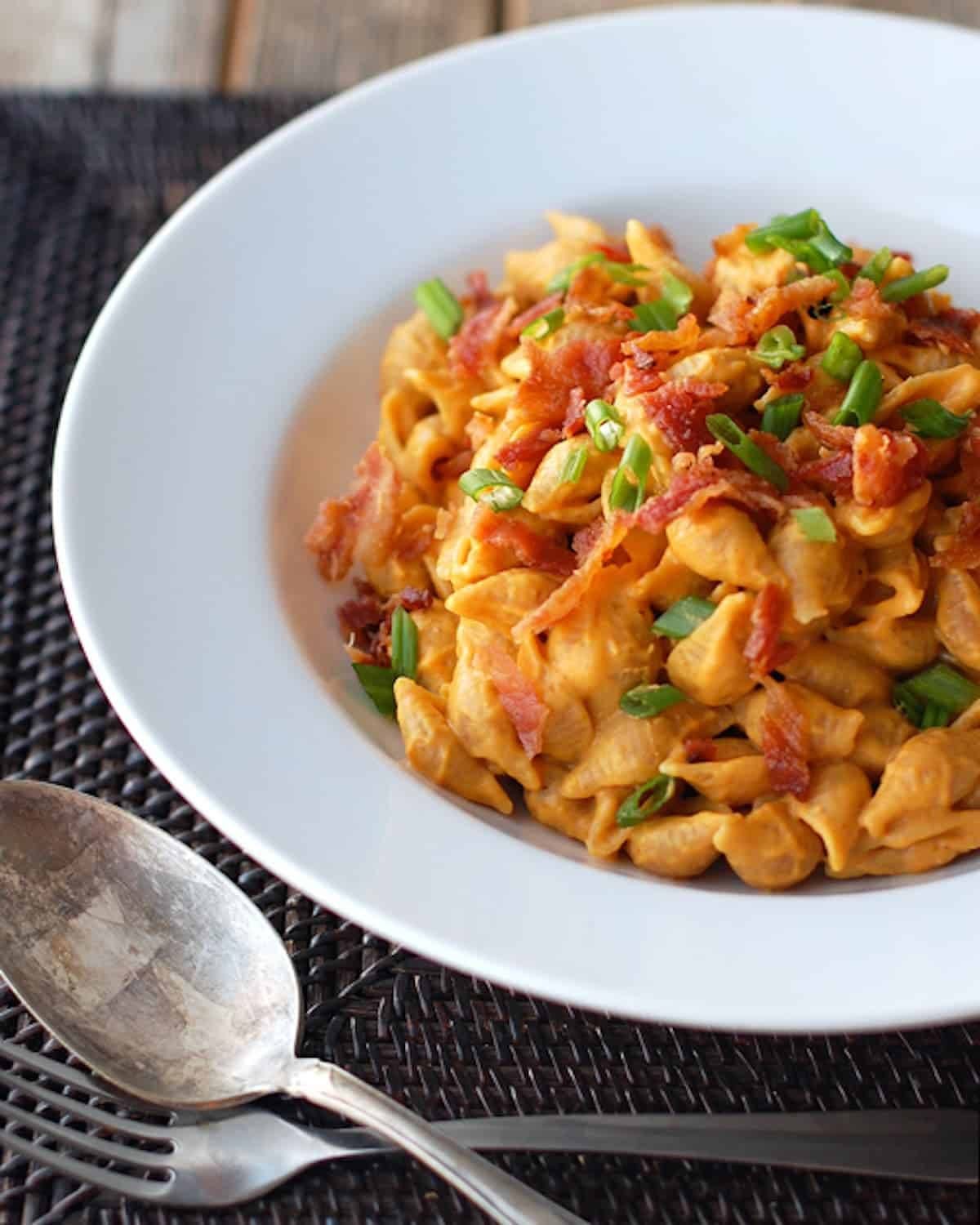 Bacon and pumpkin pasta with creamy pumpkin sauce, whole wheat pasta shells, and crumbled bacon in a white bowl with a spoon and a fork.