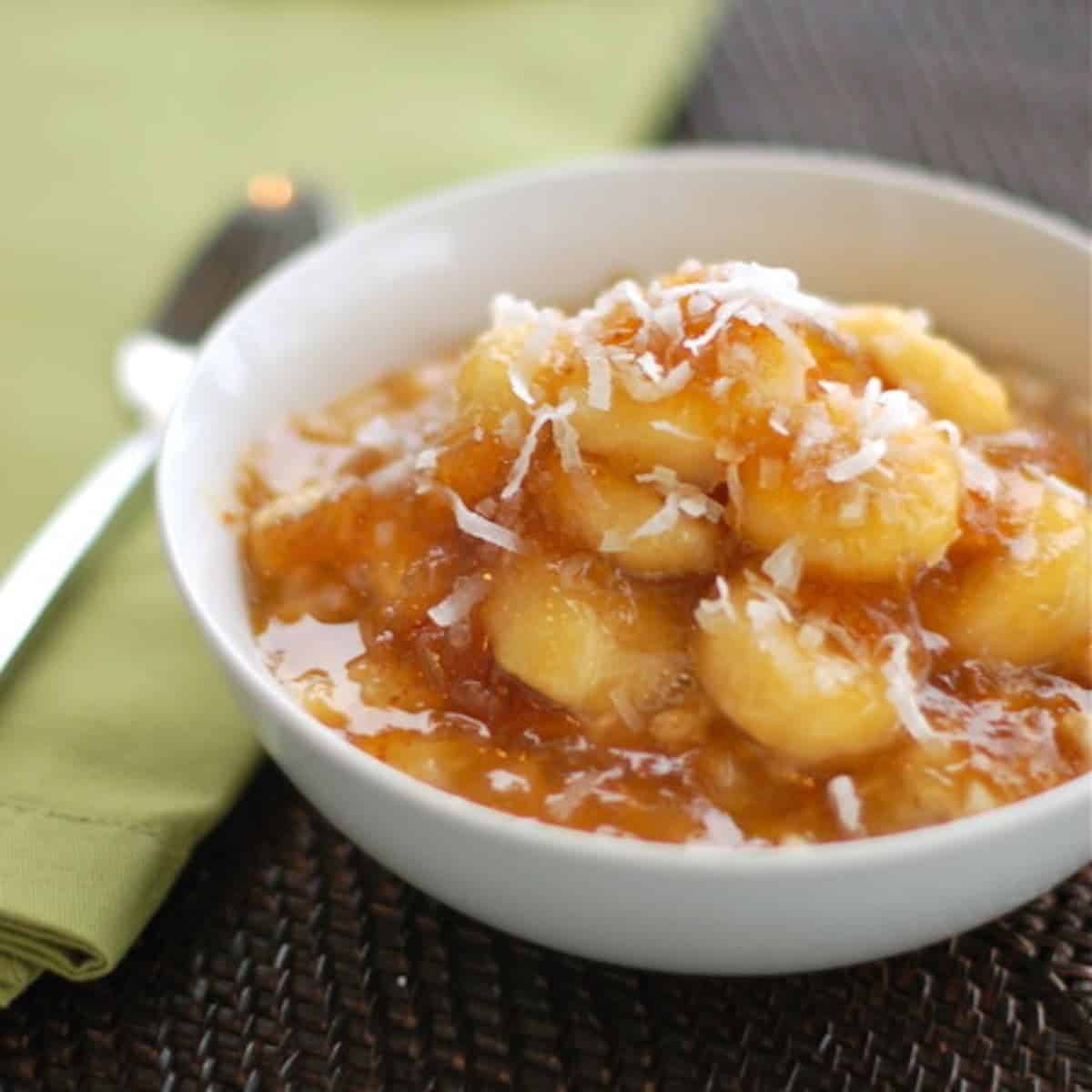 Caramelized banana and fig oatmeal in a white bowl next to a green napkin and a spoon.