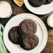 Dark chocolate cookies on a plate next to a glass of milk.