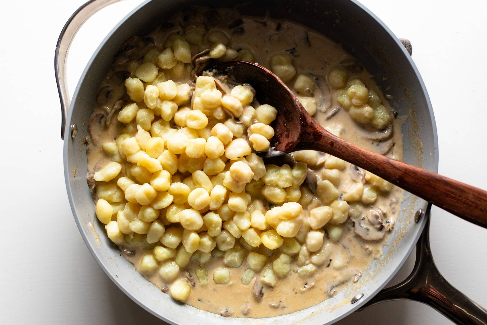 Adding mushroom to a pan with sauce.