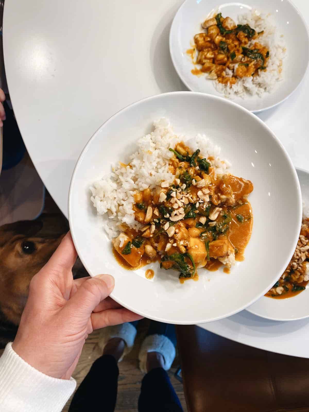 A hand holds a plate of rice, sauce and meat over other dishes.